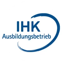 Rundes Logo mit blauem Schriftzug „IHK Ausbildungsbetrieb“; rechts daneben verläuft ein breiter, halbkreisförmiger Pinselzug in dunklerem Blau, der die Worte optisch umrahmt. Das Zeichen signalisiert, dass der Betrieb offiziell von der Industrie- und Handelskammer als Ausbildungsbetrieb anerkannt ist.